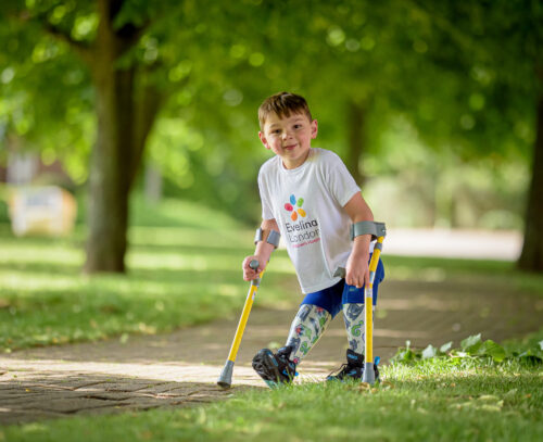Young boy Tony smiles at camera in the park. He is using crutches