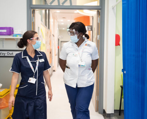 Two nurses walk and talk inside a hospital