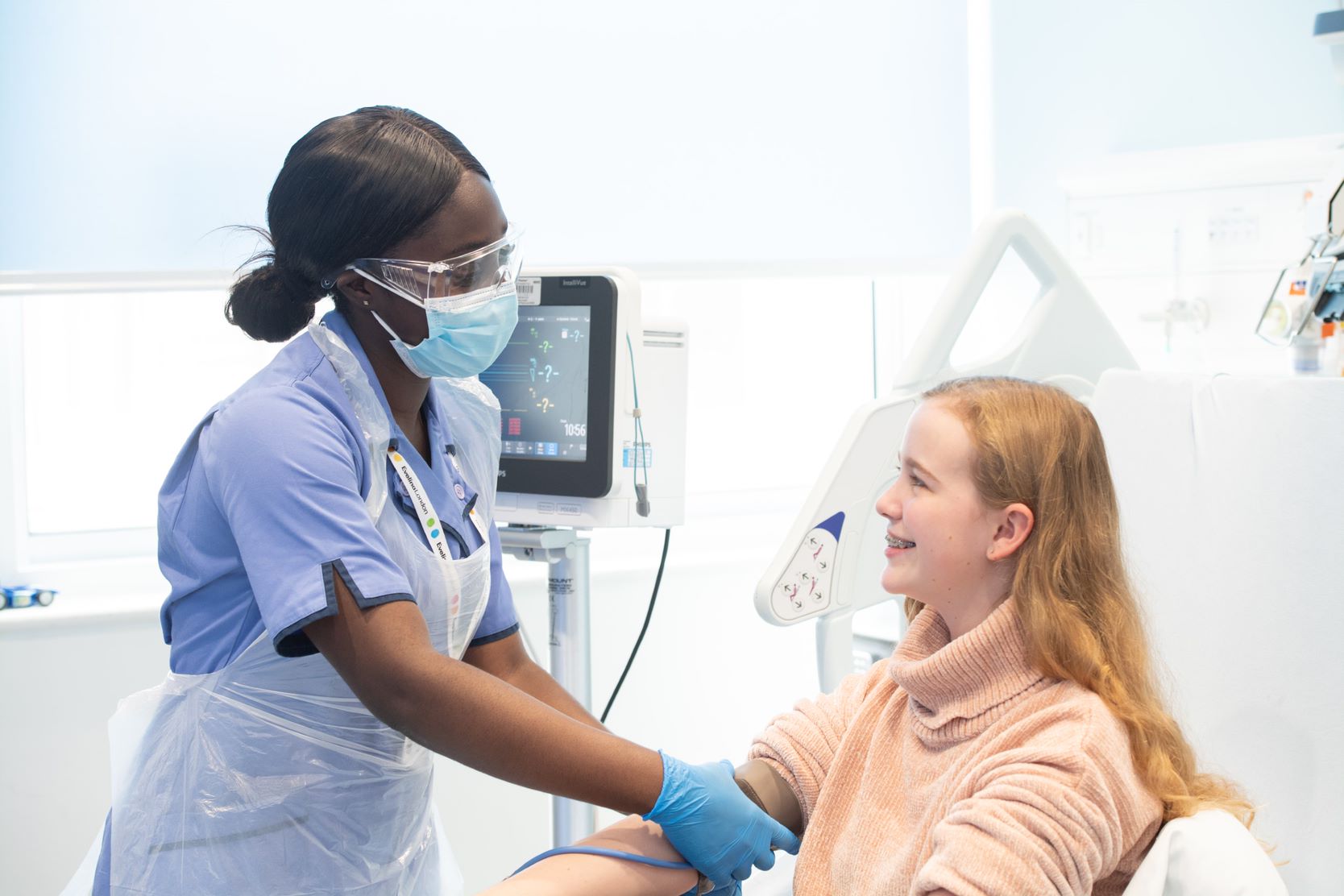 Hospital worker speaks to girl smiling in hospital bed