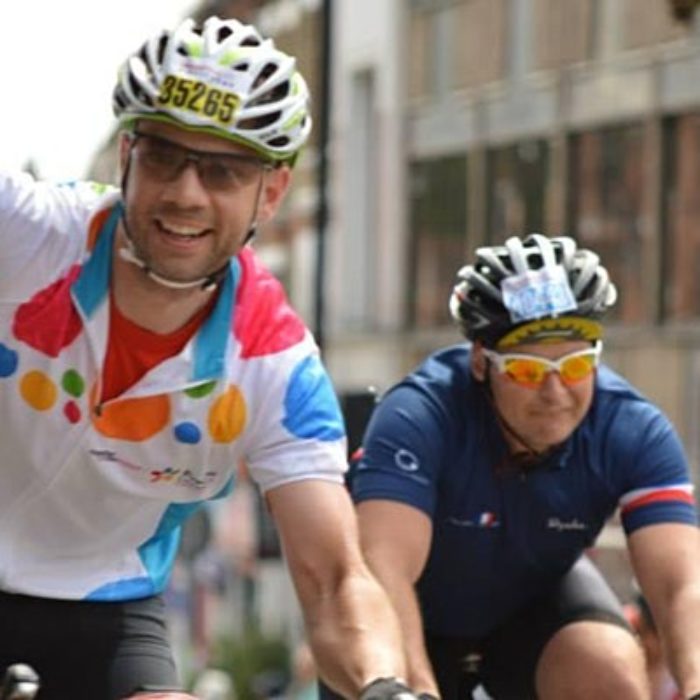 Two cyclists taking part in event. One waves to the camera.
