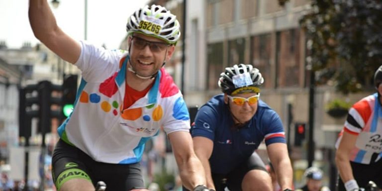 Two cyclists taking part in event. One waves to the camera.