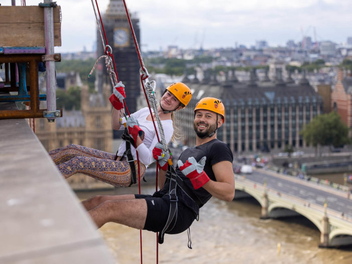 Male and female abseiler give thumbs up while dangling off building