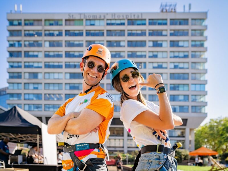 Alex and Selena, both Evelina London Children's Charity supportersm they're both wearing a white top and helmets, behind them is St Thomas' Hospital they're about to abseil down.