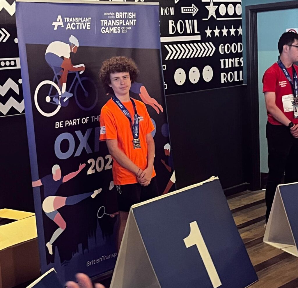 Henry Hair who appears to be smiling in an orange t-shirt with is medal as he got first place at British Transplant Games. He