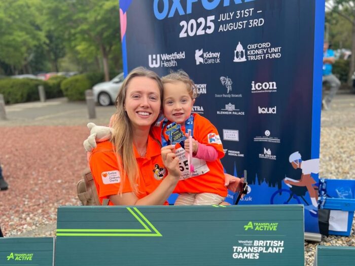 Mum, Laura holding her little girl Gloria who is holding up her medal. Both are in bright orange shirts and on Laura