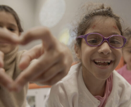 Image of three smiling girls, one making a heart sign with her hands