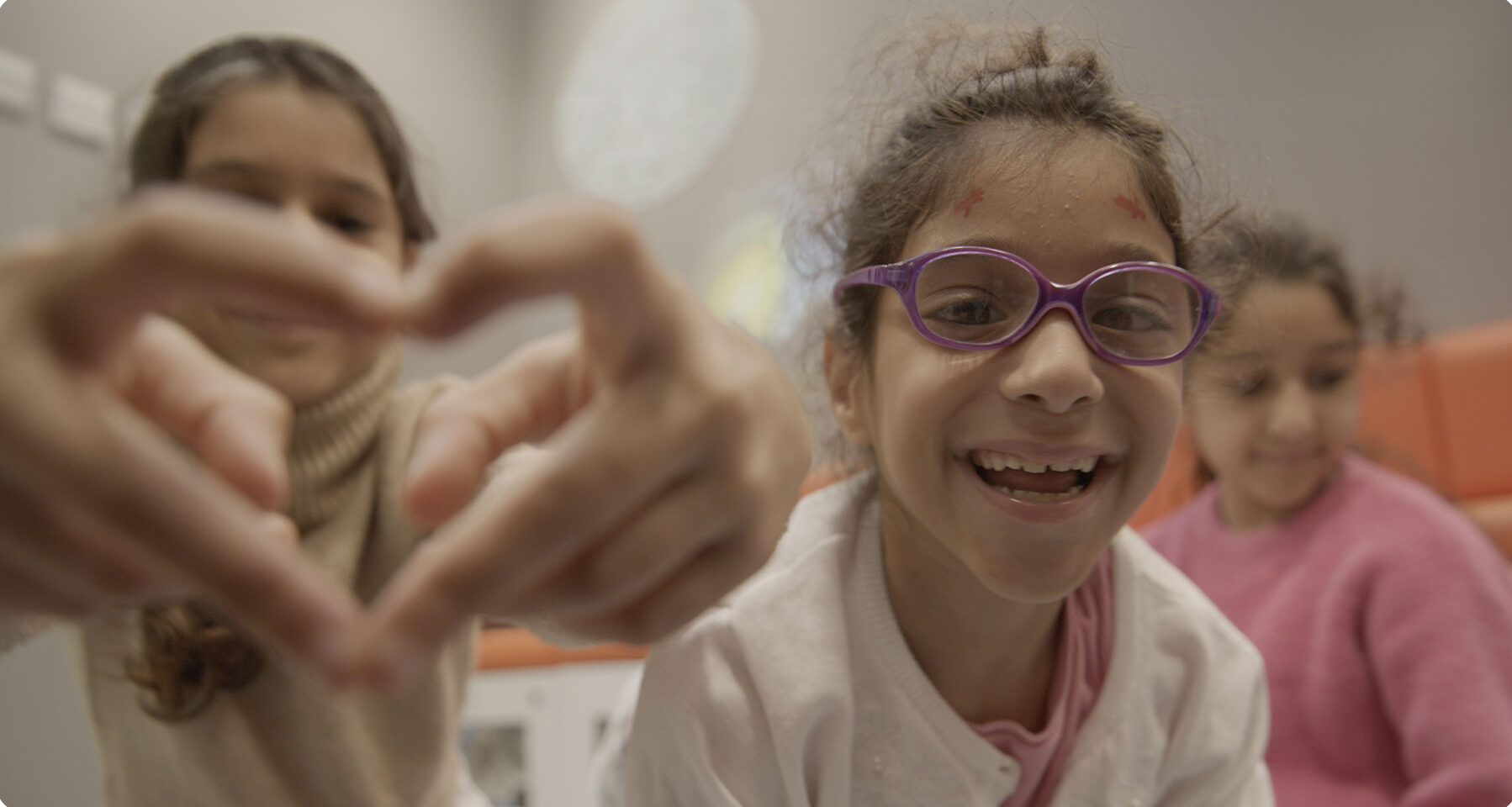 Image of three smiling girls, one making a heart sign with her hands