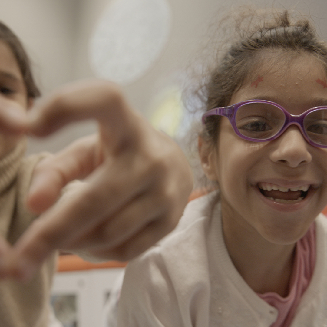 Image of two girls smiling, one making a heart sign with her hands