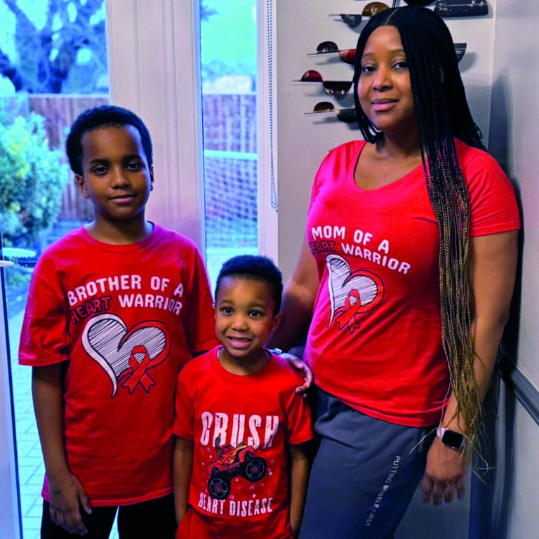 Little boy Hamza with his mum and older brother all wearing red t shirts smiling in front of window.