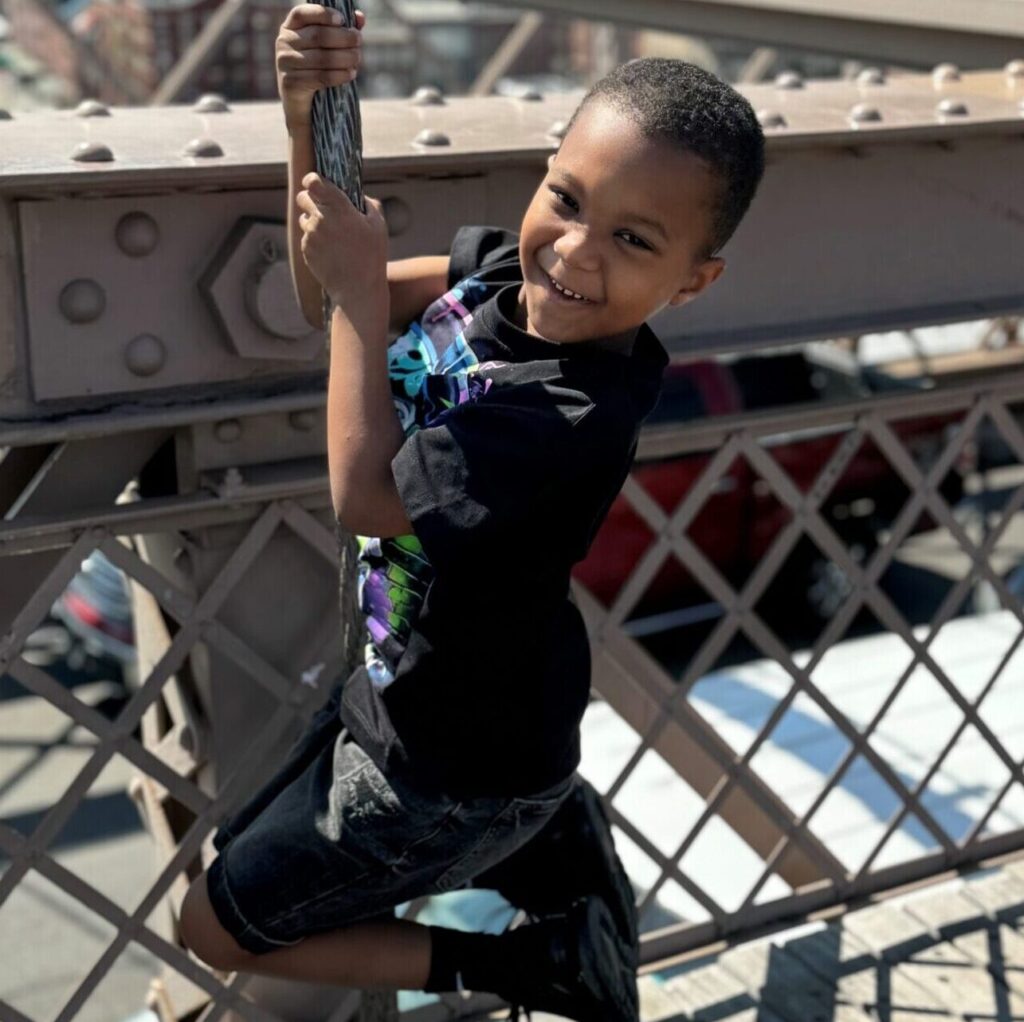 Hamza smiling wrapped around a metal pole with metal fencing behind him.