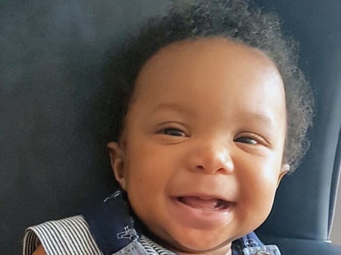 Baby Hamza smiling in a striped t shirt with navy dungarees.