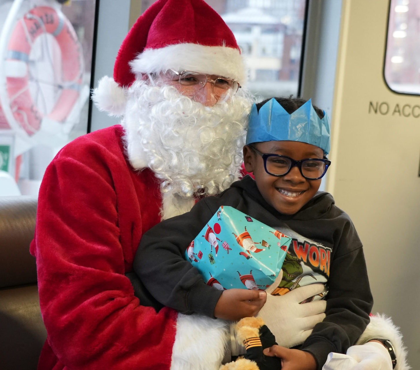 Santa giving a little boy wearing a blue paper crown a present on Thames Clipper.