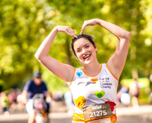 Woman running Royal Parks Marathon with arms up to make a heart shape.