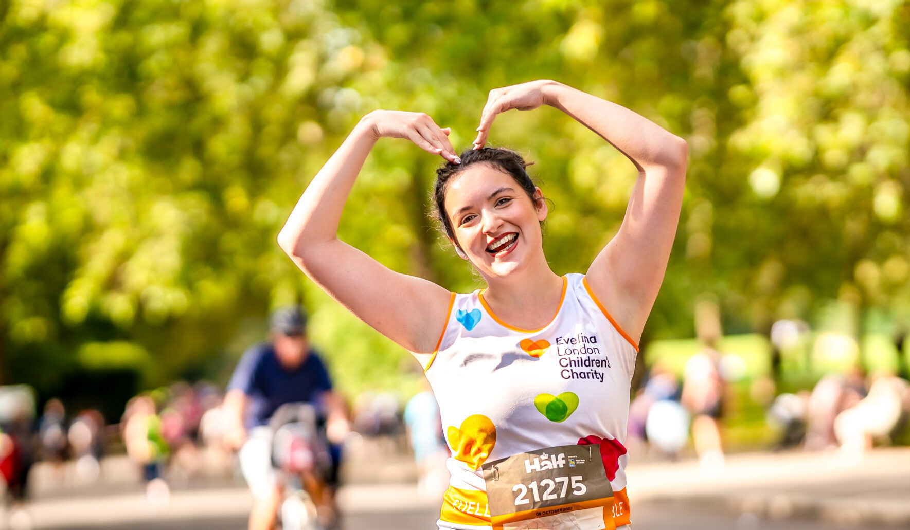 Woman running Royal Parks Marathon with arms up to make a heart shape.