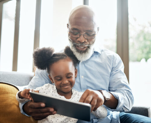 A little girl using a digital tablet with her grandfather at home.