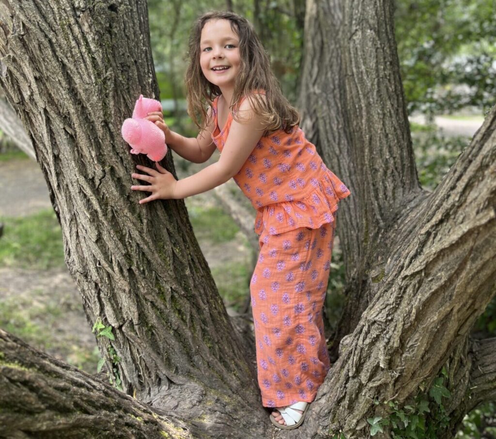 Indy amongst two trees holding a pink cuddly toy wearing a pink printed top and trouser co-ord.