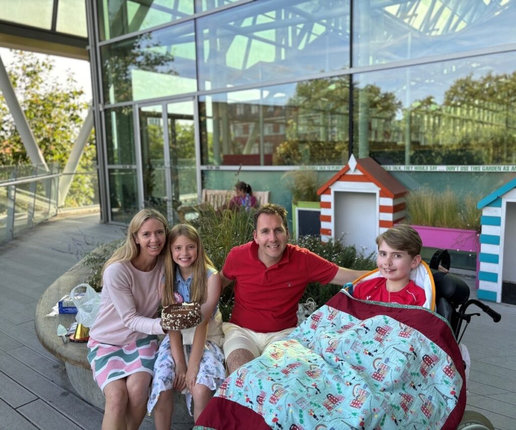 Austin with his dad, mum and sister smiling outside of Evelina London Children