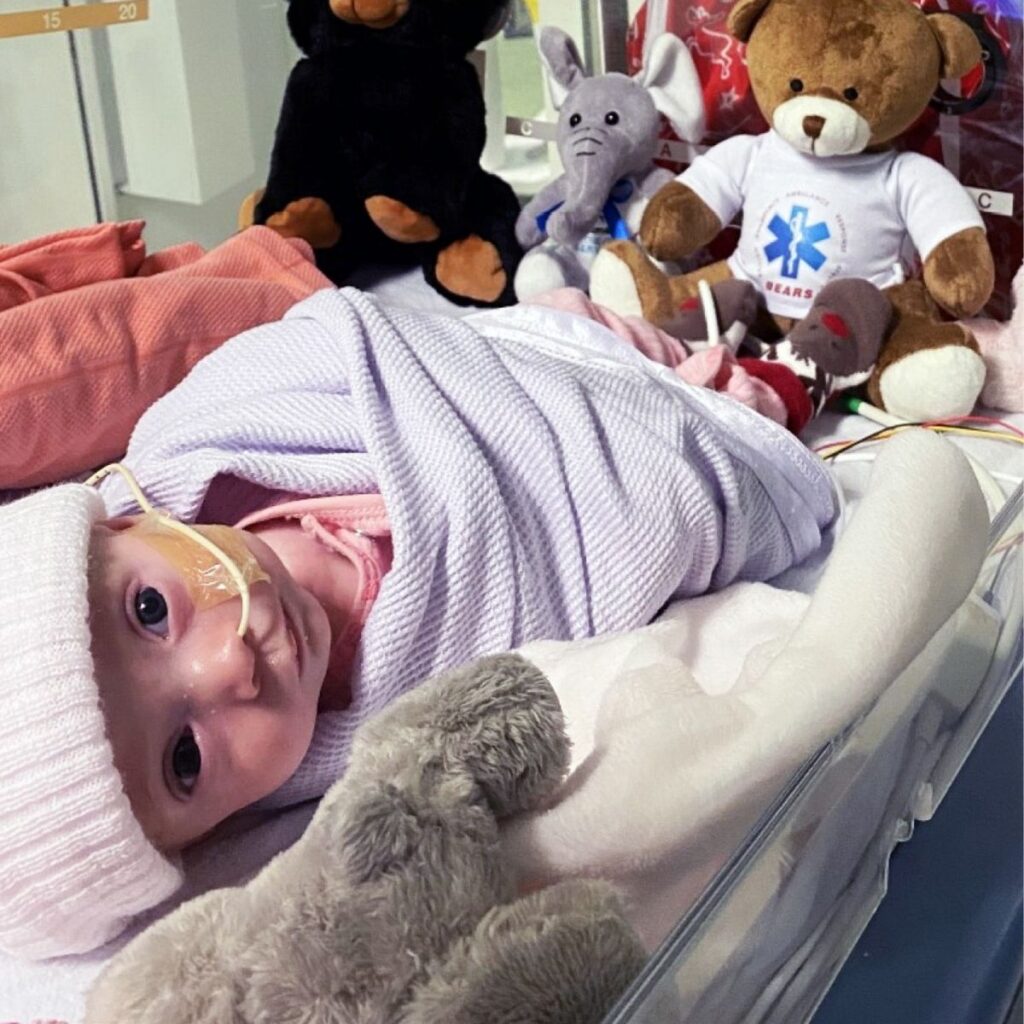 Baby Molly is in critical care unit cot, surrounded by plush toys.