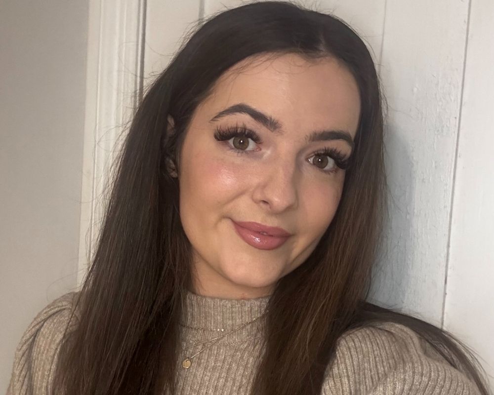 Danielle with long brown hair appears to be smiling, wearing a light brown jumper.