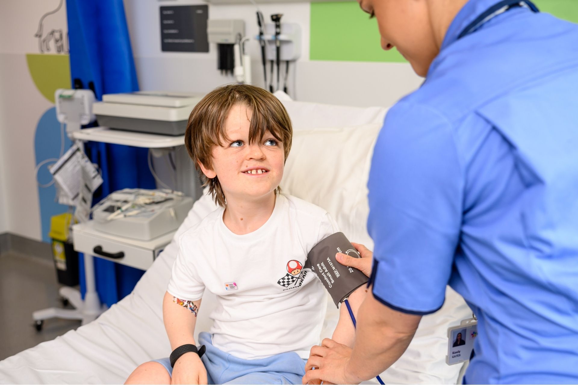 Oliver getting his blood pressure measured on Evelina London Children's Hospital bed, nurse it taking his blood pressure and features the back of her in blue uniform.