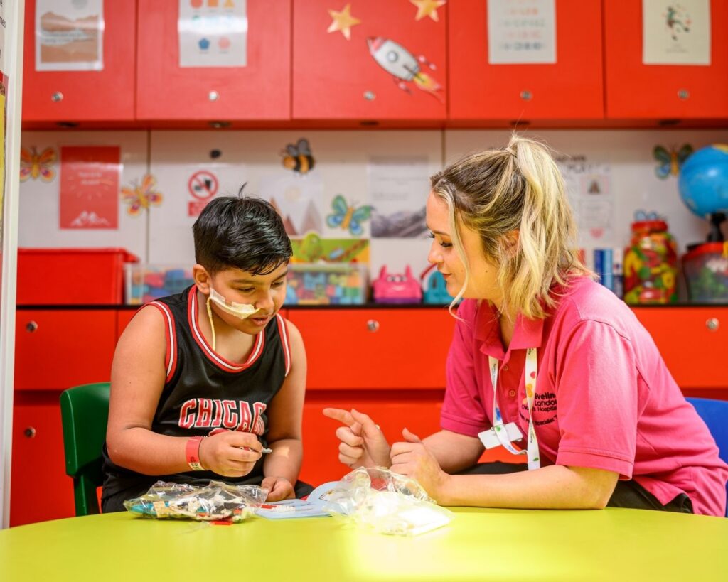 Veer sat with play specialist, Jess looking at instructions to construct a toy at Evelina London Children