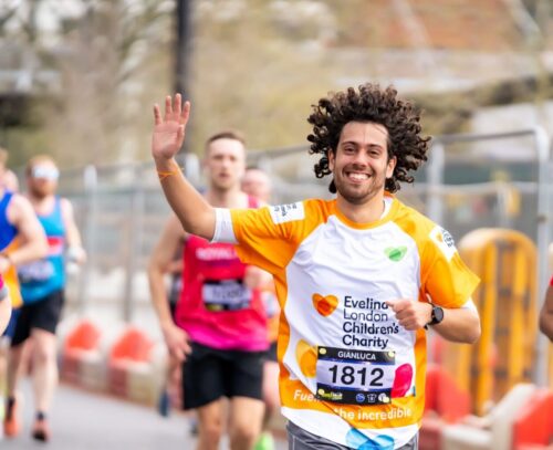 Evelina London Charity Supporter running in a marathon alongside other runners. He appears to be smiling and waving, wearing an orange Evelina London Children