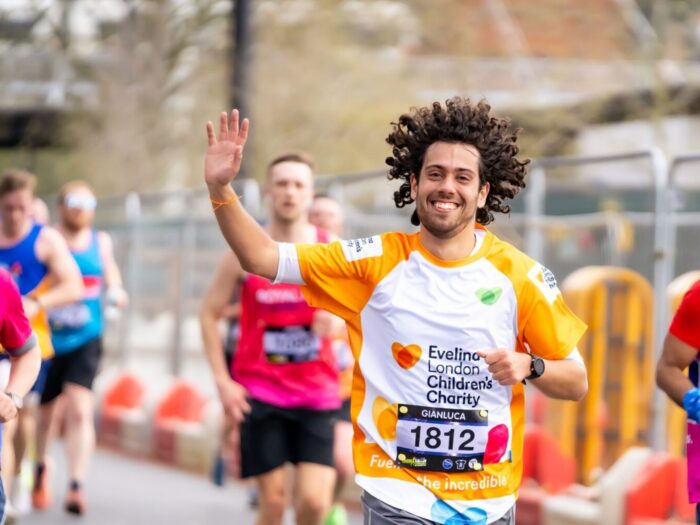Evelina London Charity Supporter running in a marathon alongside other runners. He appears to be smiling and waving, wearing an orange Evelina London Children