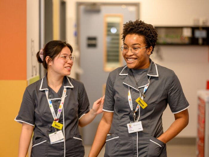 Two Evelina London members in grey uniform with white piping on their collars, they appearing to be smiling.