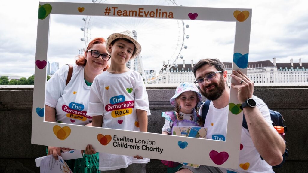 Holman family taking part in The Remarkable Race, in the background is London Eye, Clint on the right and Kerry on the left holding up a frame that reads 