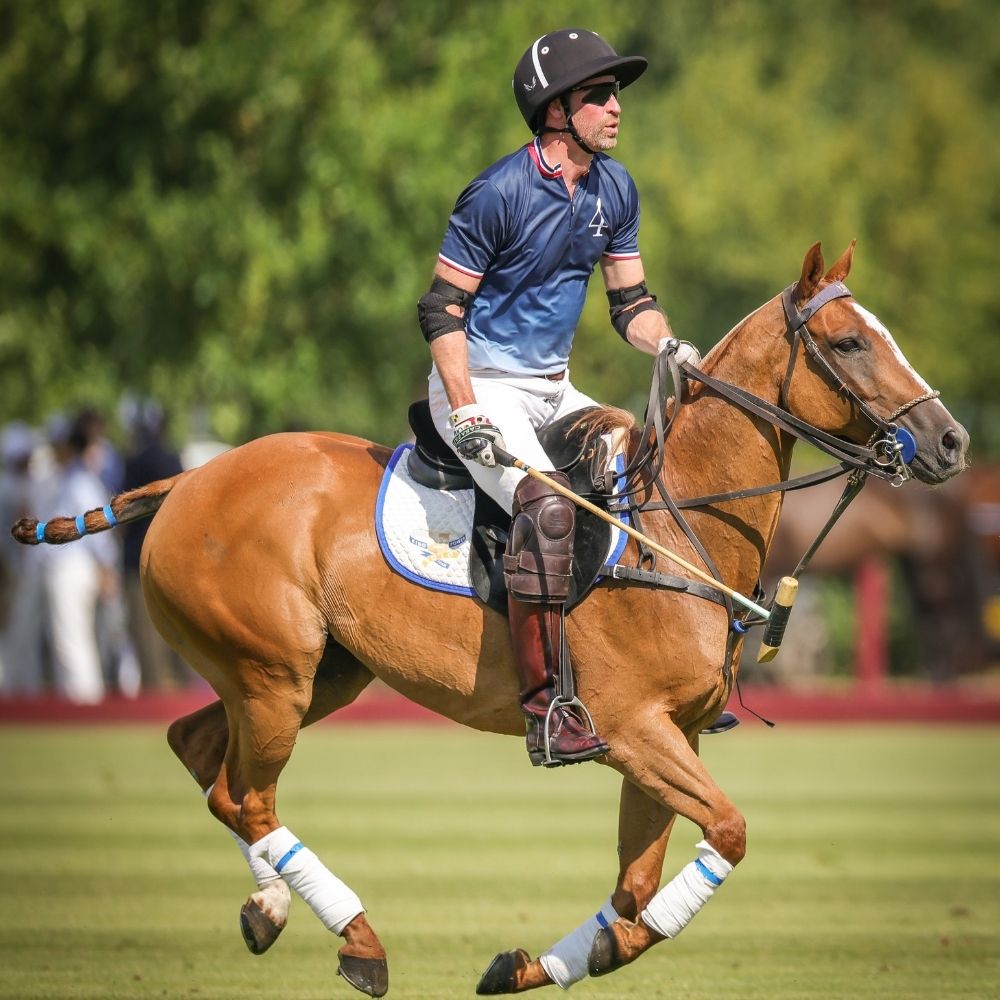 His Royal Highness The Prince of Wales competing at the polo fundraiser on a brown horse.